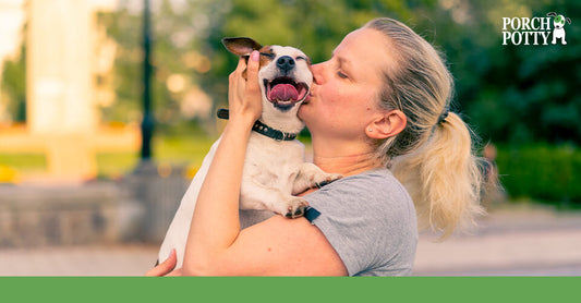 A woman lovingly kissing her small dog while it happily smiles with its tongue out.